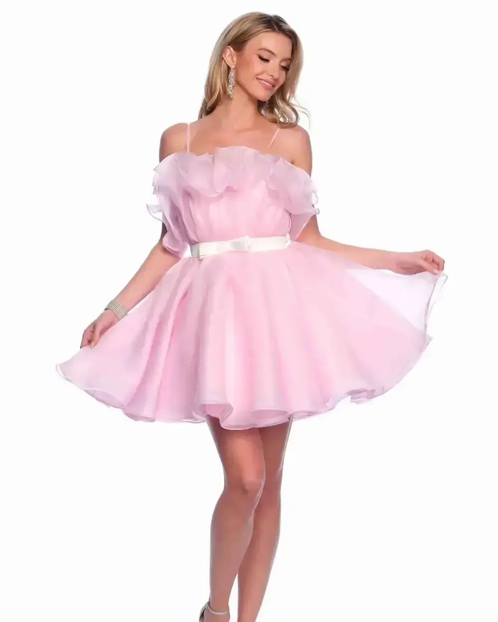 A woman in a light pink off-shoulder dress with ruffles, holding the hem of the dress and smiling.