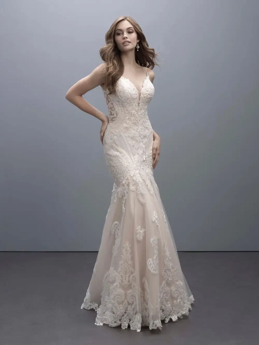 A model wearing a stunning bridal gown with intricate lace details and a fitted silhouette, posed gracefully against a gray background.