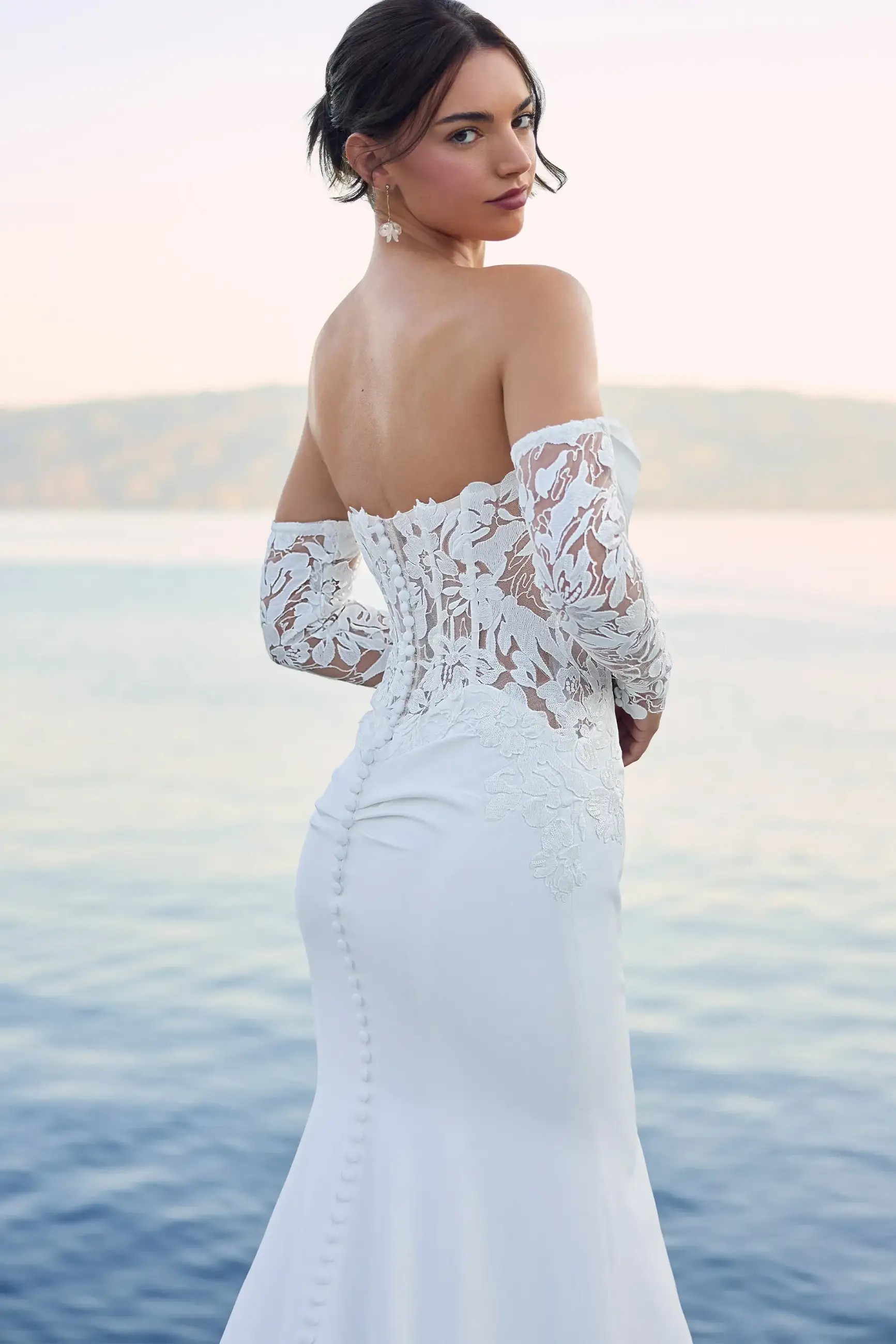 Model is wearing a crepe floral lace wedding dress with a scoop neckline by enchanting by mon cheri 